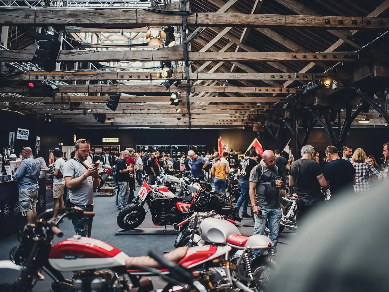 A group of motorcyclists admiring motorcycles in a large wooden shed